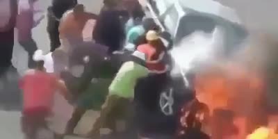 people remove man from car about to catch fire