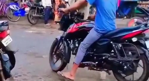 A man tries to ride a bike while a langur monkey is sitting on it
